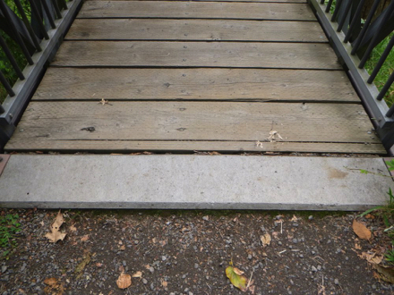 Transition from gravel trail onto wooden bridge with railing may have a lip